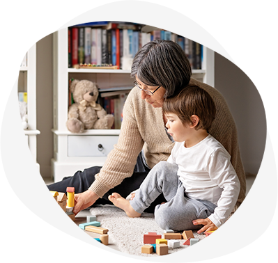 Little toddler boy playing wooden building blocks with grandmother at home. Family spending time together at quarantine period during pandemic. Bright lifestyle_