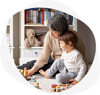 Little toddler boy playing wooden building blocks with grandmother at home. Family spending time together at quarantine period during pandemic. Bright lifestyle_